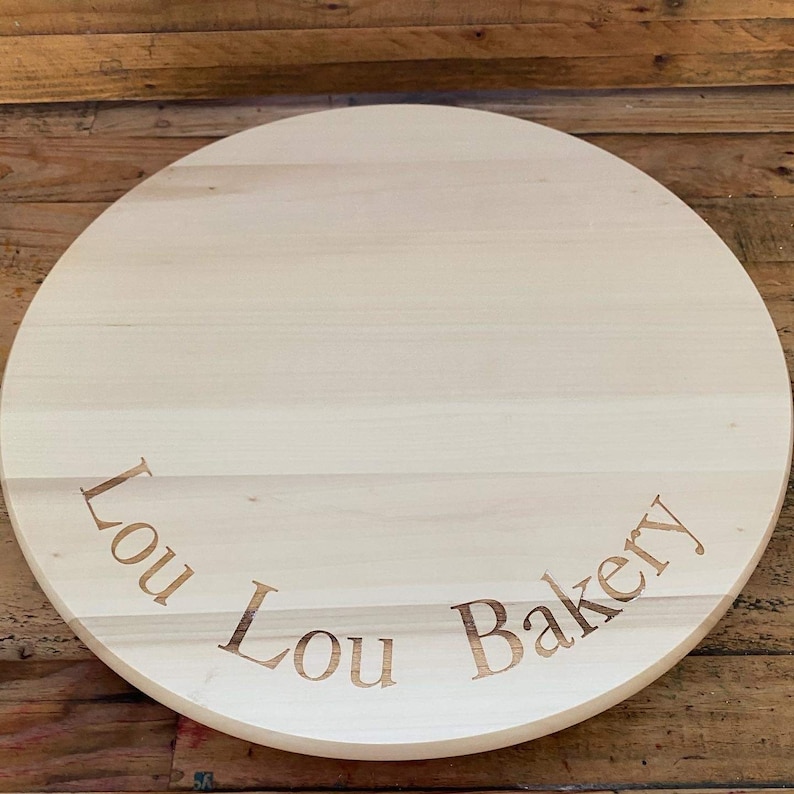 以下が含まれることがあります： 「Lou Lou Bakery」と刻まれた丸い木のケーキボードです。