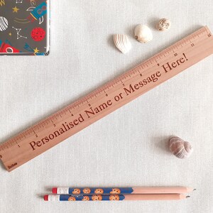 Op de afbeelding: Een houten liniaal met een bruine afwerking en een witte achtergrond. De liniaal is 30,5 cm lang en heeft markeringen voor elke centimeter. De liniaal heeft de tekst "Gepersonaliseerde naam of bericht hier!" erop gegraveerd.