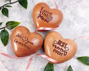 May include: Three wooden heart-shaped ornaments with engraved messages. One says "Love you Mum", another "We love you Grandma", and the third "Best Mummy ever!". Each heart is light brown with a pink ribbon.