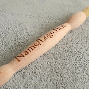 May include: A wooden brush with a natural bristle head. The handle is engraved with the text "Name/Logo Here".