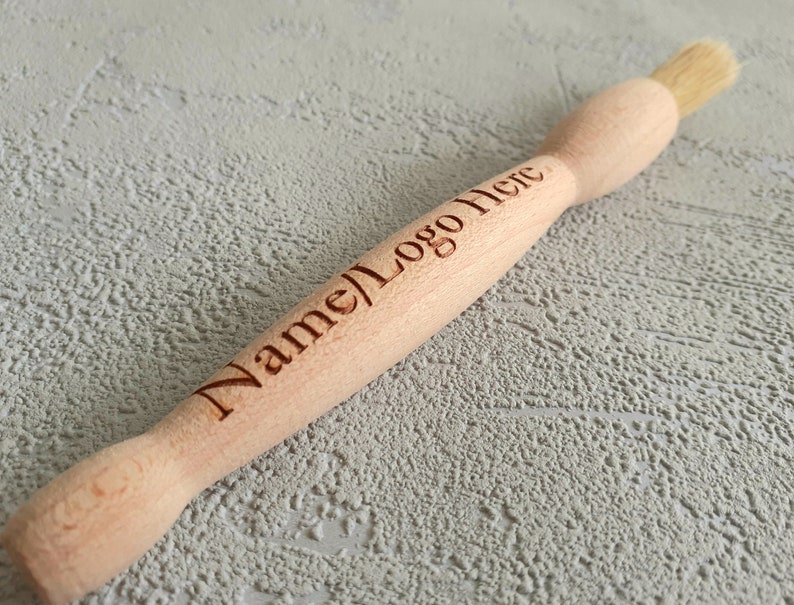 May include: A wooden brush with a natural bristle head. The handle is engraved with the text "Name/Logo Here".
