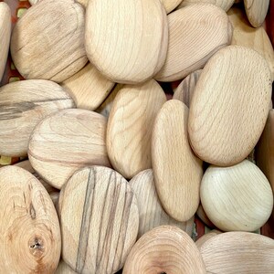 Puede incluir: Primer plano de una pila de piedras de madera lisas de forma ovalada. Las piedras son de color marr&oacute;n claro con vetas y patrones de grano marr&oacute;n oscuro.