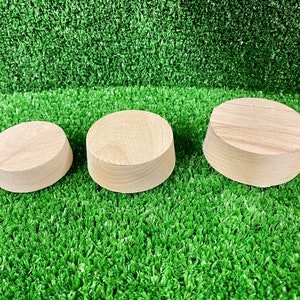 May include: Three wooden round display stands of varying sizes, arranged in a row on a green artificial grass surface.