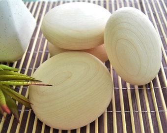 May include: Four smooth, round, wooden massage stones in a natural light wood color. The stones are arranged in a stack on a brown woven mat.