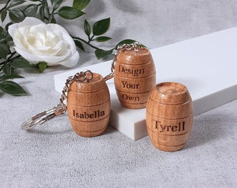May include: Three small wooden barrel-shaped ornaments with metal hardware. Two barrels feature engraved names, Isabella and Tyrell, while the third barrel is engraved with the text Design Your Own. The barrels have a light brown wood grain finish.