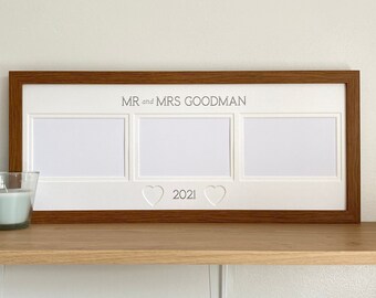 May include: A white picture frame with a brown wood frame. The frame has three openings for pictures and the text "MR and MRS GOODMAN 2021" is engraved on the bottom.