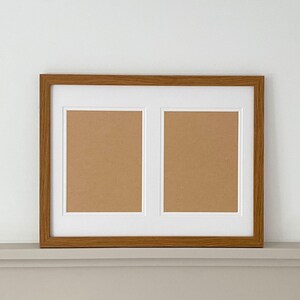 May include: A wooden picture frame with two openings for photos. The frame is light brown and has a white mount around each opening.