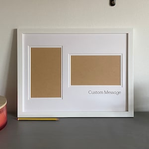 May include: White picture frame with two openings for photos. The frame has a white mount and a brown backing. The text "Custom Message" is printed below the larger opening.