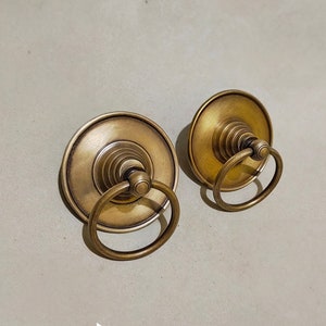 Puede incluir: Dos pomos de puerta de latón antiguo con un tirador de anillo. Los pomos tienen un diseño decorativo en capas.