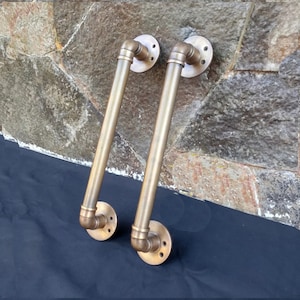 May include: Two brass door handles with a pipe design. The handles are attached to round plates with screws.