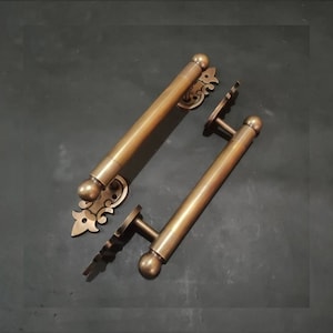 May include: Two antique brass door handles with ornate scrollwork details. The handles are cylindrical with rounded ends and feature a decorative plate with a floral design.