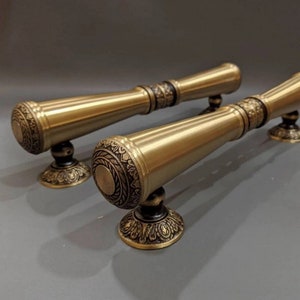 May include: Two ornate gold door handles with intricate designs. The handles are cylindrical with a rounded end and a decorative base.