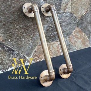 May include: Two brass industrial style door handles with a pipe design. The handles are mounted on a black surface.