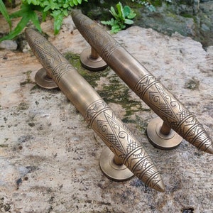 以下が含まれることがあります： 複雑な幾何学模様が施された、装飾的な真鍮製のドアノブが2つ。ノブの先端は尖っており、装飾的なベースが付いています。