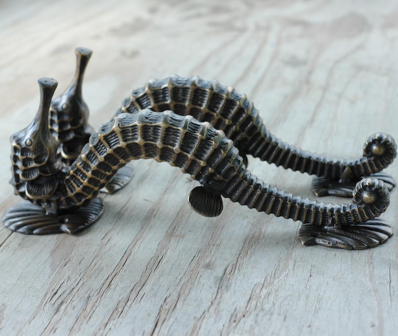 Peut inclure: Poign&eacute;es de meubles en bronze en forme d'hippocampe. Les poign&eacute;es pr&eacute;sentent un design d&eacute;taill&eacute; et textur&eacute; avec un corps incurv&eacute; et une queue enroul&eacute;e. Les hippocampes sont mont&eacute;s sur une base d&eacute;corative.