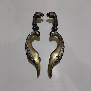 以下が含まれることがあります： 金色の仕上げと黒いアクセントが施された、装飾的なドアノブのペア。ノブは、装飾的なデザインが施されたスタイリッシュな葉の形をしており、上部に動物の頭部が特徴です。