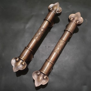 May include: Two antique-style door handles with ornate, decorative, floral-shaped ends. The handles are made of a dark, aged metal with a textured finish.