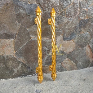 Könnte beinhalten: Zwei goldfarbene Türklinken mit einem gedrehten Design und spitzen Enden. Die Klinken sind an einer Steinwand montiert.