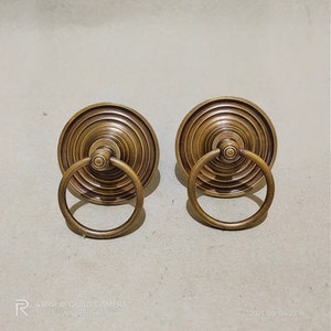 May include: Two antique brass door pulls with a ring handle. The pulls have a circular design with concentric rings.