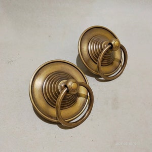 May include: Two brass door knobs with a circular ring handle and a decorative, layered, cone-shaped top.