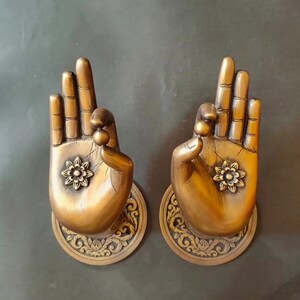 May include: Two ornate brass door handles shaped like hands in a prayer position. Each handle features a detailed floral design and a small bead at the tip of each finger.