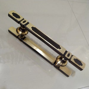 May include: A gold door handle with a black accent and a decorative design. The handle is made of metal and has a polished finish.