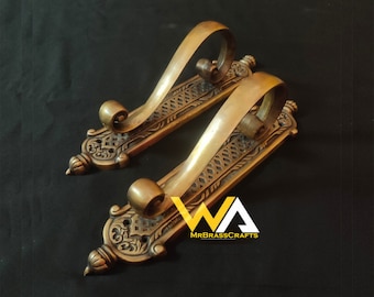 May include: Two ornate brass hooks with intricate designs and a scroll-like shape. The hooks are mounted on a flat surface and have a decorative finish.