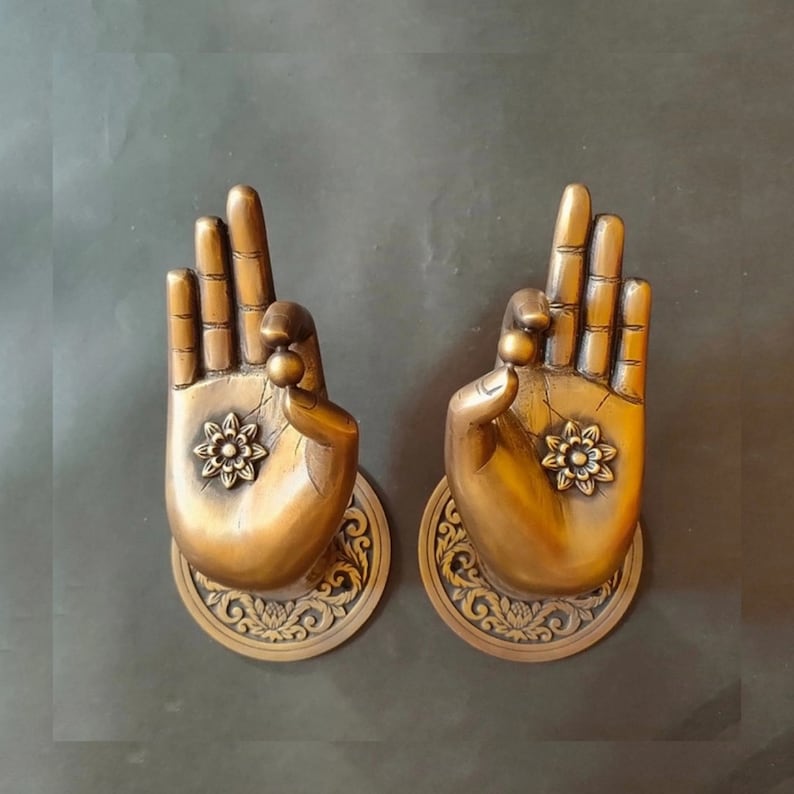 May include: Two gold-toned door handles shaped like hands in a prayer position. Each handle has a decorative flower design in the center of the palm.