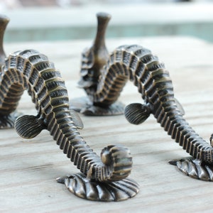 Peut inclure: Tirants de meubles en forme d'hippocampes en bronze. Ces poign&eacute;es d&eacute;coratives pr&eacute;sentent un motif d'hippocampe d&eacute;taill&eacute; avec une finition textur&eacute;e. Les hippocampes sont mont&eacute;s sur une base en forme de coquillage. Id&eacute;al pour une touche nautique.