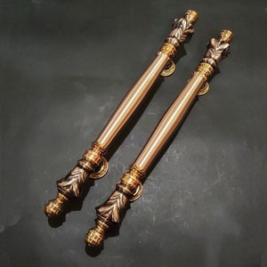 May include: Two ornate gold door handles with a decorative leaf design. The handles are made of metal and have a polished finish.