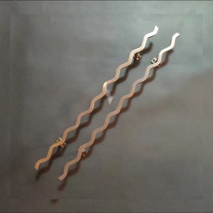 Puede incluir: Dos tiradores de puerta ondulados de metal, acabado en oro cepillado. Los tiradores están fijados a la pared con tornillos.