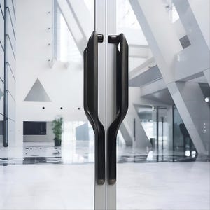 May include: A pair of glass doors featuring dark grey, contemporary door handles. The handles have a curved, ergonomic design. The background reveals a bright, white interior with geometric architectural elements.