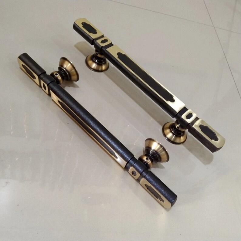 May include: Two black and gold door handles with ornate designs. The handles are made of metal and have a brushed finish.