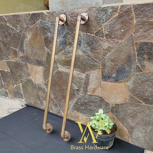 May include: Two brass door handles with a pipe design. The handles are mounted on a stone wall. Brass Hardware is written below the handles.