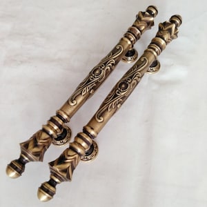 May include: A pair of ornate, antique-style door handles with a decorative, floral design. The handles are made of brass and have a warm, aged finish.