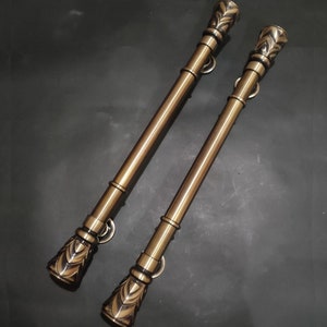 May include: Two gold-toned door handles with ornate, decorative ends. The handles are long and slender, with a smooth, polished finish.