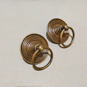 Puede incluir: Dos tiradores de puerta de latón antiguo con un diseño circular acanalado y un asa de anillo.