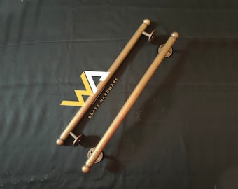 Könnte beinhalten: Zwei lange, goldfarbene Türklinken aus Metall mit abgerundeten Enden. Die Griffe sind an runden Metallplatten befestigt. Der Text "BRASS HARDWARE" ist auf einem der Griffe sichtbar.