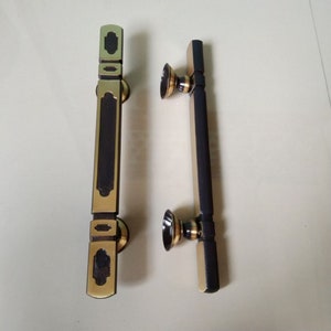 May include: Two door handles with a black and gold finish. The handles are rectangular with a decorative design.