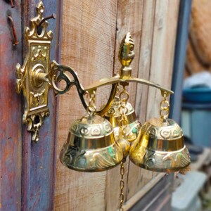 May include: A gold-toned door chime with three bells hanging from a decorative metal bracket. The bells are ornate and have intricate designs.