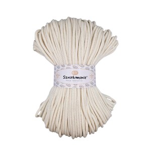 Op de afbeelding: Een close-up van een grote spoel met natuurlijke witte katoenen touw. Het touw is gemaakt van 100% katoen en is perfect voor knutselen, macramé en andere doe-het-zelfprojecten. De spoel is gelabeld met "Sznurkomania" met de tekst "Pasja tworzenia" eronder.
