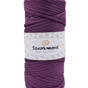 Pode incluir: Um carretel de cordão de algodão roxo, etiquetado com "Sznurkomania Pasja tworzenia" e um logotipo de um novelo de lã.