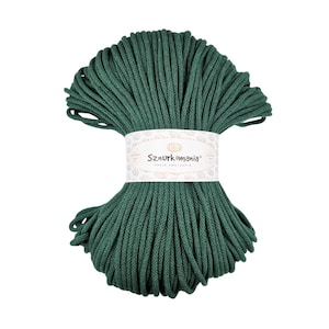 Könnte beinhalten: Eine Spule mit dunkelgrünem Baumwollgarn, umwickelt mit einem weißen Etikett mit dem Text "Sznurkomania" in braunen Buchstaben.