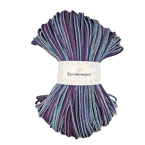 Könnte beinhalten: Ein Knäuel mehrfarbiger Baumwollschnur mit weißen, blaugrünen, violetten und marineblauen Streifen. Die Schnur ist um ein Etikett gewickelt, auf dem "Sznurkomania" mit dem Slogan "Pasja tworzenia" steht.
