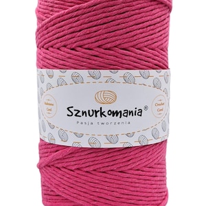 Puede incluir: Un carrete de hilo de macramé de color fucsia vibrante. El hilo está envuelto y asegurado con una etiqueta blanca con el texto "Sznurkomania" y la frase "Pasja tworzenia". La etiqueta también incluye ilustraciones de ovillos.