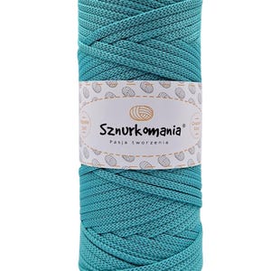 Puede incluir: Una madeja de hilo azul turquesa con una etiqueta blanca que dice "Sznurkomania Pasja tworzenia" y un pequeño círculo con las palabras "Crochet Cord".