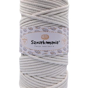 Può includere: Un gomitolo di cordoncino in cotone color avorio, etichettato "Sznurkomania" con il testo "Pasja tworzenia", che si traduce in "Passione per la creazione". Il cordoncino è adatto per progetti di macramè e uncinetto.