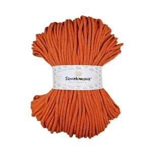 Peut inclure: Une bobine de cordon en coton orange avec une étiquette blanche sur laquelle est inscrit "Sznurkomania Pasja Tworzenia".