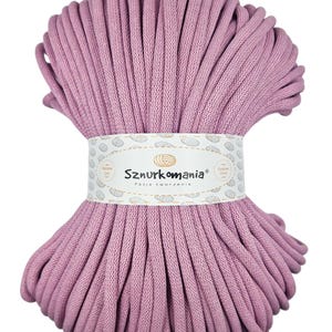 May include: A large spool of dusty rose colored cotton cord. The cord is wrapped around itself in a spiral shape. The label on the spool reads "Sznurkomania Pasja tworzenia".