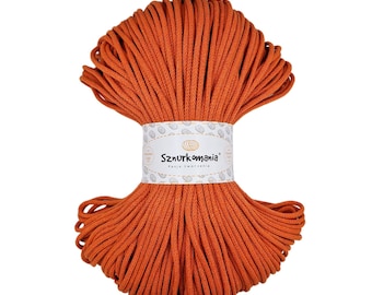May include: A bright orange skein of macrame cord, tightly wound and held together with a branded paper band. The band displays the text "Sznurkomania" and a decorative pattern. This cord is suitable for various crafting projects.